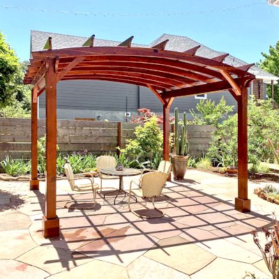 Arched Open Sky Pergolas (Options: 12' L x 14' Arc W, California Redwood, 1 Electrical Wiring Trim, 4-Post Anchor Kit for Concrete, No Ceiling Fan Base, No Privacy Panels, No Curtain Rods, 9.5' Post Height, Transparent Premium Sealant). Custom decorative steel shading added by customer. Photo was taken one year after installation. Photo Courtesy of K. Cates of Oajland, California.