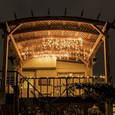 Arched Pergola Kit (Options: 12' L x 16' Arc W, Mosaic Redwood, No Electrical Wiring Trim Kit, 4-Post Anchor Kit for Wood, No Ceiling Fan Bases, No Privacy Panels, No Curtain Rods, 9' Post Height, Transparent Premium Sealant). Free Standing Pergola was altered slightly to place up against house by limiting overhang on house side.
