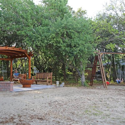 Arched Pergola Kits (Options: 12' L x 14' Arc W, California Redwood, Electrical Wiring Trim for 1 Post, 4-Post Anchor Kit for High-Wind, No Ceiling Fan Base, No Privacy Panels, No Curtain Rods, 9' Post Height, Transparent Premium Sealant). With 2 Bench Swings by Custom Request. Photo Also Shows a Rory's Swing Set and a Ti Amo Bench. Photo Courtesy of Tom Marten of Kitty Hawk, North Carolina.