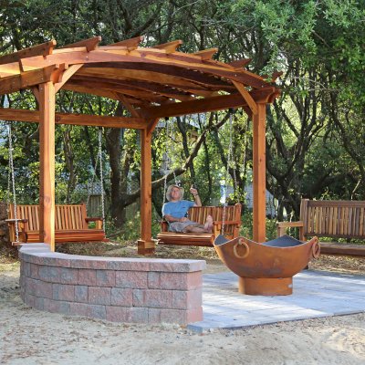 Arched Pergola Kits (Options: 12' L x 14' Arc W, California Redwood, Electrical Wiring Trim for 1 Post, 4-Post Anchor Kit for High-Wind, No Ceiling Fan Base, No Privacy Panels, No Curtain Rods, 9' Post Height, Transparent Premium Sealant). With 2 Bench Swings by Custom Request. Photo Also Shows a Ti Amo Bench. Photo Courtesy of Tom Marten of Kitty Hawk, North Carolina.