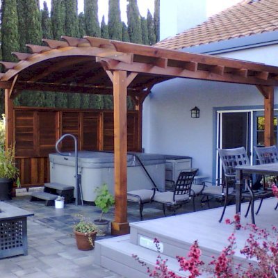 Arched Pergola Kits (Options: 15' L x 16' Arc W, California Redwood, Electrical Wiring Trim for 1 Post, 4-Post Anchor Kit for Stone, No Ceiling Fan Base, 1 Shutter Privacy Panel half height with wall, No Curtain Rods, 9' Post Height, Transparent Premium Sealant). Photo Courtesy of James Nimmo of Vacaville, CA.