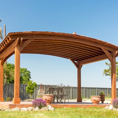 Custom Arched Thick Timber Pavilion (Options: 14' L x 20' Arc W, Mature Redwood, 1 Electrical Wiring Trim, 4-Post Anchor Kit for Concrete, No Ceiling Fan Base, No Privacy Panel, No Curtain Rods, 9 ft H, with 2x6's Roof Boards by Custom Request, Coffee-Stain Premium Sealant). Photo Courtesy of Siino Ventures of Kikrland, Washington.