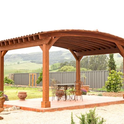 Custom Arched Thick Timber Pavilion (Options: 14' L x 20' Arc W, Mature Redwood, 1 Electrical Wiring Trim, 4-Post Anchor Kit for Concrete, No Ceiling Fan Base, No Privacy Panel, No Curtain Rods, 9 ft H, with 2x6's Roof Boards by Custom Request, Coffee-Stain Premium Sealant). Photo Courtesy of Siino Ventures of Kikrland, Washington.
