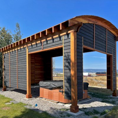 Custom  Arched Thick Timber Pavilion (Options: 28' L x 18' Arc W, California Redwood, Post Anchor Kit for High-Wind, with Custom Privacy Walls, 10' & 12' H Posts, No Curtain Rods, Walls Siding with Black Stain and the Rest of the Structure with Transparent Premium Sealant). Photo Courtesy of D. Harris of Tetonia, ID.