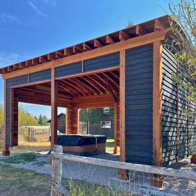 Custom  Arched Thick Timber Pavilion (Options: 28' L x 18' Arc W, California Redwood, Post Anchor Kit for High-Wind, with Custom Privacy Walls, 10' & 12' H Posts, No Curtain Rods, Walls Siding with Black Stain and the Rest of the Structure with Transparent Premium Sealant). Photo Courtesy of D. Harris of Tetonia, ID.