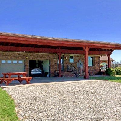 Custom Arched Thick Timber Pavilion (Options: 55' L x 22' Arc W, California Redwood, No Electrical Wiring Trim, 6-Post Anchor Kit for High-Wind, 2 Ceiling Fan Bases, No Privacy Panel, No Curtain Rods, 10ft H, Cherry Stain Premium Sealant) Support timbers covered by custom request. Photo also shows a Round Picnic Table. Photo Courtesy of J. Hartmann of Pittsburg, KS.