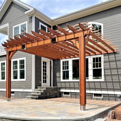 Custom Attached Garden Pergolas (Options: 20' L x 21' W, Attached to Wall by Support Side, Mature Redwood, Champion Timber End Cut, Electrical Wiring Trim for 2 Posts, 1 Ceiling Fan Base, Open Roof with Slats at 12", Rafters at 18", No Rain Guard, Vertical Post Decorative Trims, 12' H Posts, 2-Post Anchor Kit for Concrete, Transparent Premium Sealant). Trim boxes that hide the anchors were installed after the photo was taken.