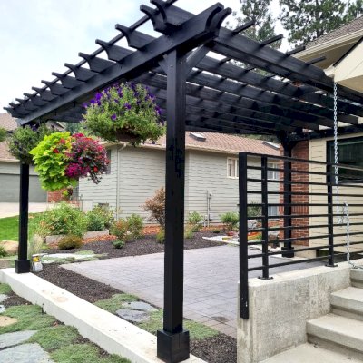 Custom Attached Garden Perglola (Options: Trapezoid Roof Shape [19' Front, 12' Back, 20' Deep], Mosaic Douglas-Fir, Open Roof with Slats at 18", Rafters at 18", with 3 Posts by Custom Request, No Rain Guard, 3-Post Anchor Kit for Concrete, No Privacy Panel, No Ceiling Fan Base, Black Stain Premium Sealant). Photo Taken 1 Year After Installation [After Resealed]. Photo Courtesy of T. Perko of Spokane, WA.