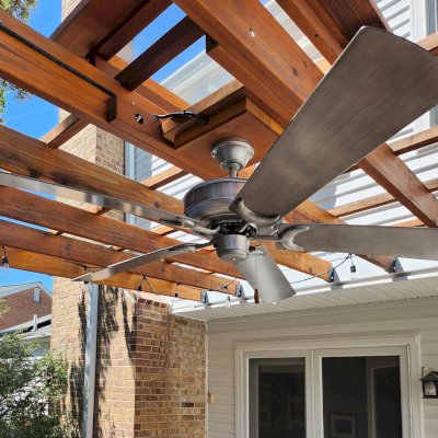 Attached Garden Pergola (Options: 18' x 15', California Redwood, Open Roof with Slats at 18", Rafters at 18", 2-Post Anchor Kit for Concrete, 1 Ceiling Fan Base, Transparent Premium Sealant). Custom framed 2' x 2' Polycarbonate Rain Guard centered atop ceiling fan base to protect fan from moisture. Photo Taken 6 Months After Installation. Photo Courtesy of M. Holland of Potomac, Maryland.