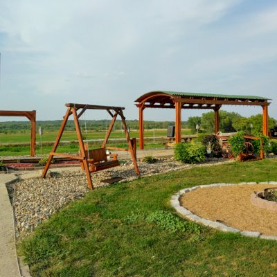 Backyard Pavilion Kits (Options: 20' x 12'-6", California Redwood, No Electrical Wiring Trim Kit, 4-Post Anchor Kit for Concrete, 1 Ceiling Fan Base, No Privacy Panels, No Curtain Rods, 10 ft Post Height, Transparent Premium Sealant) with a Sheldon's Monkey Bar and a Rory's Armchair Swing. Photo Courtesy of Jody & Bob Purdie of Mitchellville, Iowa.