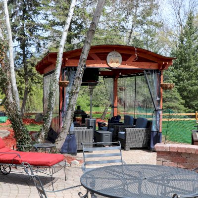 Custom Backyard Pavilion Kit with Extra Supports and Braces on Arches Side (Options: 16' L x 12' Arc W, Douglas-fir, 1 Post Electrical Wiring Trim, 4-Post Anchor Kit for High-Wind, 1 TV Mount Base by Custom Request, No Privacy Panels, No Curtain Rods, 9 ft Post Height, Cherry-Stain Premium Sealant). Photo Courtesy of E. Chen of Ann Arbor, Michigan.