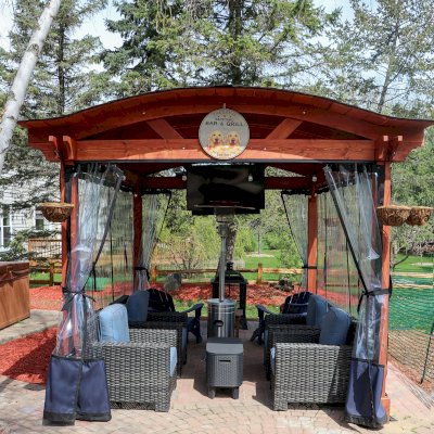 Custom Backyard Pavilion Kit with Extra Supports and Braces on Arches Side (Options: 16' L x 12' Arc W, Douglas-fir, 1 Post Electrical Wiring Trim, 4-Post Anchor Kit for High-Wind, 1 TV Mount Base by Custom Request, No Privacy Panels, No Curtain Rods, 9 ft Post Height, Cherry-Stain Premium Sealant). Photo Courtesy of E. Chen of Ann Arbor, Michigan.