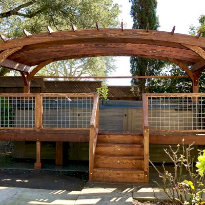 Custom Arched Pergola Kits (Options: 12' L x 22' Arc W, Douglas-fir, Unattached, Electrical Wiring Trim Kit for 1 Post, Arched Roof with Lattice Panels and Acrylic Sheets Centered, 4-Post Anchor Kit for Stone, with 8 x 8 Posts by Custom Request, No Ceiling Fan Base, No Privacy Panels, 1 Curtain Rod, 9' Post Height, Coffee-Stain Premium Sealant) with Custom Deck and Stairs by Custom Request. Photo Courtesy of Steve & Heidi Jones of Windsor, CA.