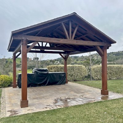 Custom Del Norte Outdoor Kitchen Pavilion (Options: 16' L x 16' W, Douglas-fir, No Privacy Panel, Post Anchor Kit for High Wind, 9.5' H Posts, No Ceiling Fan Base, 4 Electrical Wiring Trims, No Curtain Rod, Coffee Stain Premium Sealant). The color of the Coffee stain is lighter on the posts because they were refinished while the rest of the structure's finish is over a year old. Photo Courtesy of P. Boeck of Santa Rosa, CA.
