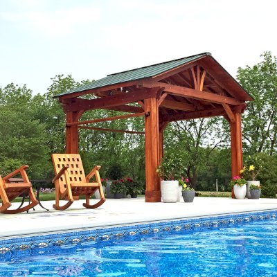 Del Norte Outdoor Kitchen Pavilionn (Options: 12' L x 14' W, Mature Redwood, 4-Post Anchor Kit for Concrete, No Ceiling Fan Base, 2 Curtain Rods, No Electrical Wiring Trim Kit, Vertical Post Decorative Trims, Transparent Premium Sealant). Extra Thick Timbers [8x8's Posts, 2x8's Rafters and 2x10's Supports] by Custom Request. Photo Also Shows 2 Lighthouse Rocking Chairs. Photo Courtesy of Sandra Briner of Westville Indiana.