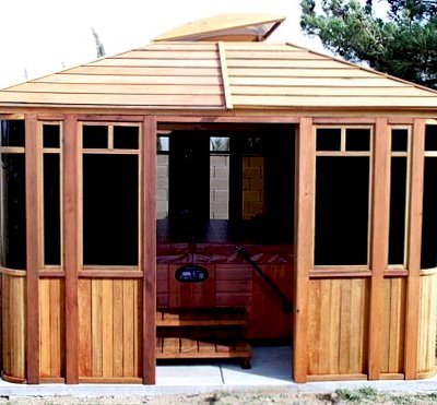 DIY Wood Gazebo (14' L, 12' W, Mature Redwood, Sliding Windows, 4' x 6' Skylight, 24" H Siding Below Windows, Vertical Siding, Japanese Doors, No Flooring, Transparent Premium Sealant). Photo also show a Spa Step inside the gazebo. Custom detail: Roof overhang was minimized per customer request.