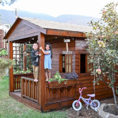Kid's Backyard Cabin (Options: 12ft L x 8ft W, 7ft Wall H, Douglas-Fir, 4ft Front Porch Size [Included in the Overall Length], Interior Decking, Transparent Premium Sealant). Photo shows structure recently resealed after 6 years of loving service.