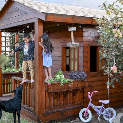 Kid's The Backyard Cabin (Options: 12ft L x 8ft W, 7ft Wall H, Douglas-Fir, 4ft Front Porch Size [Included in the Overall Length], Interior Decking, Transparent Premium Sealant). Photo shows structure recently resealed after 6 years of loving service.