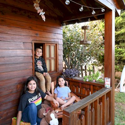 Kid's The Backyard Cabin (Options: 12ft L x 8ft W, 7ft Wall H, Douglas-Fir, 4ft Front Porch Size [Included in the Overall Length], Interior Decking, Transparent Premium Sealant). Photo shows structure recently resealed after 6 years of loving service.