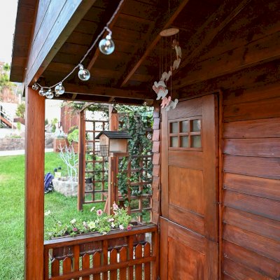Kid's Backyard Cabin (Options: 12ft L x 8ft W, 7ft Wall H, Douglas-Fir, 4ft Front Porch Size [Included in the Overall Length], Interior Decking, Transparent Premium Sealant). Photo shows structure recently resealed after 6 years of loving service.