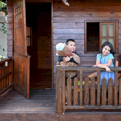 Kid's Backyard Cabin (Options: 12ft L x 8ft W, 7ft Wall H, Douglas-Fir, 4ft Front Porch Size [Included in the Overall Length], Interior Decking, Transparent Premium Sealant). Photo shows structure recently resealed after 6 years of loving service.