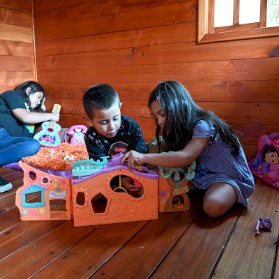 Kid's The Backyard Cabin (Options: 12ft L x 8ft W, 7ft Wall H, Douglas-Fir, 4ft Front Porch Size [Included in the Overall Length], Interior Decking, Transparent Premium Sealant). Photo shows structure recently resealed after 6 years of loving service.