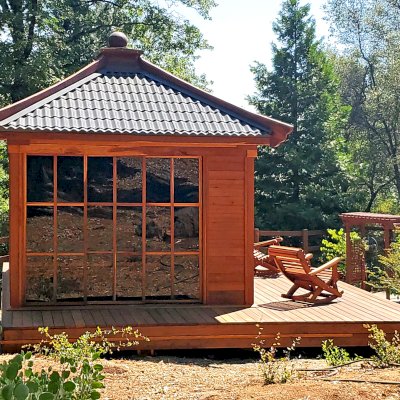 Custom Kikue's Tea House (Options: 14' x 12', 8' Wall Height, Metal Roof [Slate Gray, Metal Tile - Stile Style by bestbuymetals.com], California Redwood, with Solid Walls by Custom Request, Interior and External Decking, 6' Deck on the Front Side and 3' Decks on the Sides, Transparent Premium Sealant). Photo Also Shows 2 Ensenada Rocking Chairs. Photo Courtesy of A. Hagadron of Rough Ready, CA.