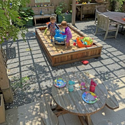 La Playa Sandbox (Options: 96"L x 60" W x 15" H, Mosaic Eco-Wood, Tongue and Grooved Lid, Transparent Premium Sealant). Photo Also Shows a Round Wooden Picnic Table for Toddlers. Photo Courtesy of M. Cooke of Westchester, IL.