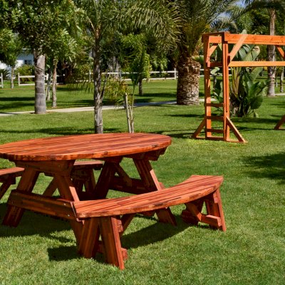 Oval Picnic Table (Options. Oval XL, Unattached Side Benches, Mosaic Redwood, Standard Tabletop, Umbrella Hole, Transparent Premium Sealant). Photo also shows a Monkey Bar in background. 
