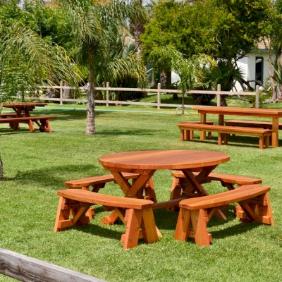 Round Wood Picnic Table with Wheels (Options: 5' Diameter, Unattached Benches,  Redwood, Round Picnic Benches, Standard Tabletop, No Lazy Susan, No Umbrella Hole, Transparent Premium Sealant). Rectangular Picnic Table and Rectangular Patio Table in background. 