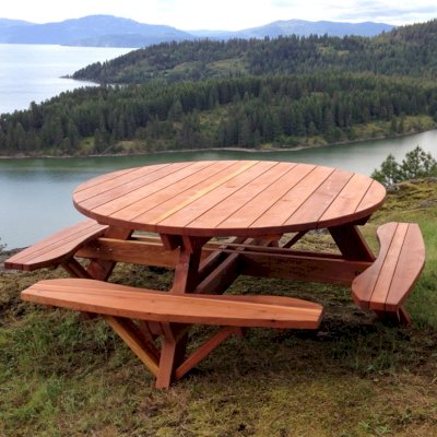 Round Wooden Picnic Tables (Attached Benches) (Options: 6' Diameter, Attached Benches, California Redwood, Standard Tabletop, No Lazy Susan, Umbrella Hole & Plug, Transparent Premium Sealant). These beautiful tables are installed at the “Bull Pine Ledge”, looking out on Lake Pend Orielle from Cloudsledge Conservation Trust, Hope Idaho. Photo Courtesy of Art Green.