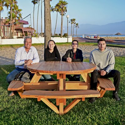Round Wooden Picnic Table (Attached Benches) (Options: 5' Diameter, Attached Benches, Mosaic Douglas-Fir, Standard Tabletop, No Lazy Susan, 2" Umbrella Hole, Transparent Premium Sealant). Photo courtesy of El Estero Beach Resort in Ensenada, Mexico.