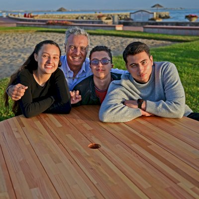 Round Wooden Picnic Table (Attached Benches) (Options: 5' Diameter, Attached Benches, Mosaic Douglas-Fir, Standard Tabletop, No Lazy Susan, 2" Umbrella Hole, Transparent Premium Sealant). Photo courtesy of El Estero Beach Resort in Ensenada, Mexico.