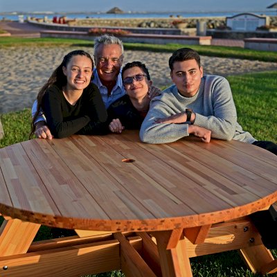 Round Wooden Picnic Table (Attached Benches) (Options: 5' Diameter, Attached Benches, Mosaic Douglas-Fir, Standard Tabletop, No Lazy Susan, 2" Umbrella Hole, Transparent Premium Sealant). Photo courtesy of El Estero Beach Resort in Ensenada, Mexico.