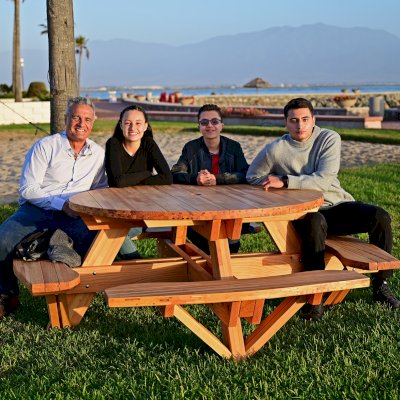 Round Wooden Picnic Table (Attached Benches) (Options: 5' Diameter, Attached Benches, Mosaic Douglas-Fir, Standard Tabletop, No Lazy Susan, 2" Umbrella Hole, Transparent Premium Sealant). Photo courtesy of El Estero Beach Resort in Ensenada, Mexico.