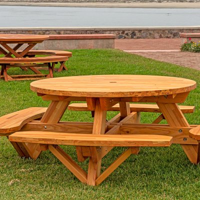 Round Wooden Picnic Table (Attached Benches) (Options: 5' Diameter, Attached Benches, Mosaic Douglas-Fir, Standard Tabletop, No Lazy Susan, 2" Umbrella Hole, Transparent Premium Sealant). Photo Shown a Kary's Folding Table Set in the Background. Photo courtesy of El Estero Beach Resort in Ensenada, Mexico.