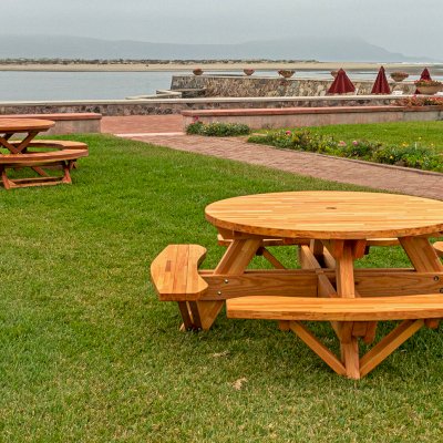 Round Wooden Picnic Table (Attached Benches) (Options: 5' Diameter, Attached Benches, Mosaic Douglas-Fir, Standard Tabletop, No Lazy Susan, 2" Umbrella Hole, Transparent Premium Sealant). Photo Shown a Kary's Folding Table Set in the Background. Photo courtesy of El Estero Beach Resort in Ensenada, Mexico.