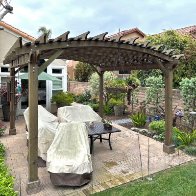 Sebastopol Pergola (Options: 14' L x 14' Arc W, Mature Redwood, 2 Electrical Wiring Trims, 4-Post Anchor Kit for Concrete, No Ceiling Fan Base, 9' Post Height, Transparent Premium Sealant). The photo shows a Pergola that is 10 years old and has no maintenance. The photo is Courtesy of J. Cheetham of Laguna Niguel, CA.