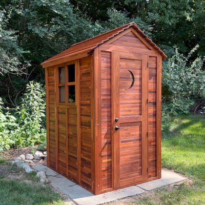 Storage Mini Barns (Options: 6' W, 4.5' D, 8' H, Mosaic Mature Redwood, Single Door, with 2 Ventilation Windows with Screens by Custom Request, 1 Shelf, Deck Flooring, Transparent Premium Sealant). Crescent Moon Cutout was Optional Request by Customer. Photo Courtsy of S. & K. Ehrsam of Washington, IL.