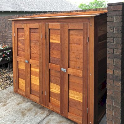 Storage Shed (Options: 8' W, 2' D, 5' H, California Redwood, Double Doors Opening Out From Center, Three Shelves at 18" H, 36" H and 50" H, Hardware Kit for Wood, Transparent Premium Sealant). Photo Taken When Rain Started. Photo Courtesy of J. Foster of Great Bend, Kansas.