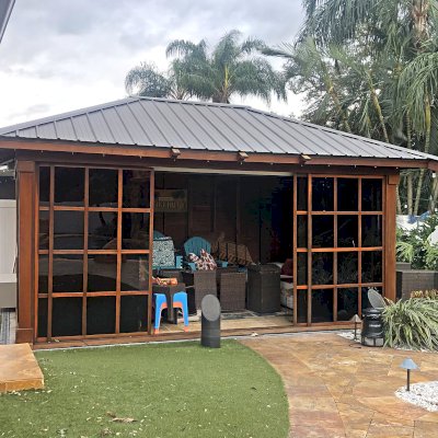 Sun Gazebo with Sliding Doors (Options: 18' L x 12' W, California Redwood, 8 ft Wall Height, Without Skylight, with 2 Sliding Walls and Two Fixed Wood Wall, Without Floor, Transparent Premium Sealant). Gazebo Was Full of Stuff Because it Was Used to Store Lawn Furniture and Other Yard Things During Hurricane Milton. Photo Courtesy of M. Skatik of Oldsmar, FL.