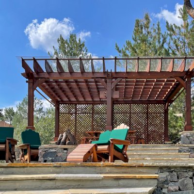 Montvale Pergolas (Options: 24' x 16', Mature Redwood, 6-Post Anchor Kit for Concrete, 1 Ceiling Fan Base and 1 T.V. Base, 2 Curtain Rods, 1 Lattice Privacy Panel, 9.5' H Posts, with Rain Guard, Coffee-Stain Premium Sealant). Photo Also Shows Some Adirondack Chairs with Ottoman. Photo Taken 1 Year After Installation, and After Restaining. Photo Courtesy of J. Brinkman of Castle Rock, Colorado.