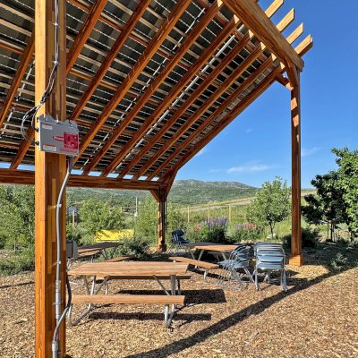 Solar Pergola (Options: 23' L x 18' W, Mosaic California Redwood, 12:7 Pitch, Post Anchor Kit for High-Wind, Transparent Premium Sealant). Pergola Installed in Colorado Mountain College in Steamboat Springs, CO.