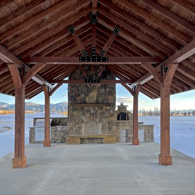 Custom Thick Timber Toledo Wood Pavilion (Options: 50' L x 24' W, Douglas-fir, 8-Post Anchor Kit for High-Wind, No Electrical Wiring Trim Kit, 10 x 8 Supports, 10 x 10 Posts & 2 x 8 Rafters, 4' Overhang by Custom Request, with 20" x 8' Cutout on the Back to Fit Fireplace, Coffee-Stain Premium Sealant). Photo Courtesy of G. Hileman of Grand Lake, Colorado.