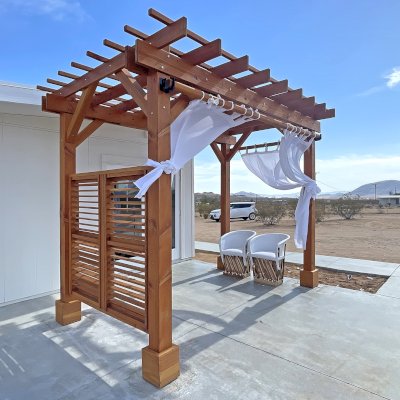 Traditional Wooden Garden Pergola (Options: 12' L x 8' W, Douglas-fir, No Electrical Wiring Trim, Open Roof with Slats at 12", Rafters at 18", with Rain Guard,  4-Post Anchor Kit for High-Wind, No Ceiling Fan Base, 1 Louver Privacy Panel Half Height Without Wall, 2 Curtain Rods, Flush End Cut Detail, 9' Posts, Transparent Premium Sealant). Photo Courtesy of E. Clay of Landers, CA.