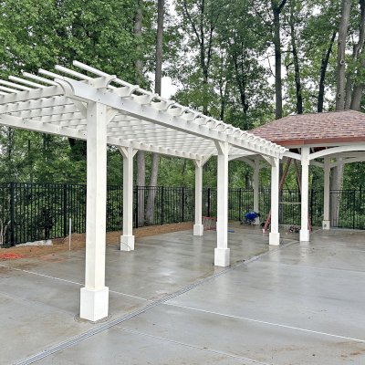 Traditional Wooden Garden Pergola (Options: 31' L x 12' W, Douglas-Fir, Electrical Wiring Trim for 4 Posts, Open Roof with Slats at 12", Rafters at 18", Post Anchor Kit for Concrete, No Ceiling Fan Base, No Privacy Panels, No Curtain Rods, 10' Posts, 8x8 Posts, White Stain Premium Sealant). Photo Also Shows a Loreto Pavilion in the Background. Photo Courtesy of Wildwood Manor Pool in Bethseda, MD
