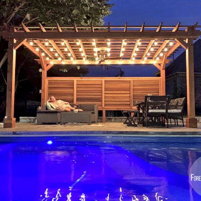 Traditional Wooden Garden Pergola (Options: 18' L x 12' W, California Redwood, 1 Electrical Wiring Trim, Open Roof with Slats at 12", Rafters at 18", Lengthwise Roof Support Timbers, 4-Post Anchor Kit for Concrete, No Ceiling Fan Base, 1 Louver Privacy Panel Half Height Without Wall, 1 Curtain Rods, 9' Post Height, Transparent Premium Sealant). Photo Courtesy of Sasha Antskaitis of Louisville, Kentucky.