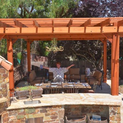 Garden Pergola Attached to a 18' x 18' Backyard Pavilion (Options: 14' L x 9' W, Mature Redwood, Electrical Wiring Trim for 1 Post, Open Roof with Slats at 18", Rafters at 18", Lengthwise Roof Support Timbers, 6 Post Anchor Kit for High-Wind, 2 Ceiling Fan Base, No Privacy Panels, No Curtain Rods, 10' Post Height, Transparent Premium Sealant). Photo Courtesy of J. Angwin of Morgan Hill, CA.