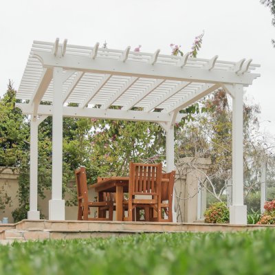 Traditional Wooden Garden Pergola (Options: 13' L x 12' W, Douglas-fir, 1 Electrical Wiring Trim, Open Roof with Slats at 6", Rafters at 18", 4-Post Anchor Kit for Concrete, No Ceiling Fan Base, No Privacy Panels, 1 Electrical Wiring Trim Kit, 9' Posts, Off-White Oil-Based Primer). Photo Also Shows a San Francisco Patio Table with Chairs in Mature Redwood. Photo Courtesy of J. Schulte of Laguna Niguel, CA.