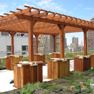 Typical Roof Top Installation: Traditional Wooden Garden Pergola (Options: 26' L x 18' W, Mature Redwood, No Electrical Wiring Trim, Rafters at 18" and Slats at 18", Lengthwise Roof Support Timbers, 6-Post Anchor Kit for Stone, No Ceiling Fan Base, No Privacy Panels, No Curtain Rods, 9' Post Height, Transparent Premium Sealant). Custom Request: 2 Extra Post. No leak roof installation using planters with concrete. NYC skyline in background.